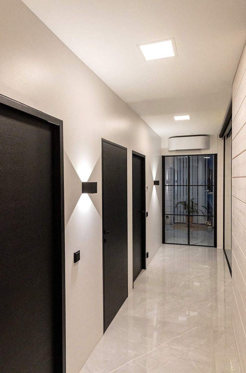 The corridor is uniformly illuminated by Paneeli 300 ceiling lights and black FUNK wall lights with a sharp green light pattern up and down.
